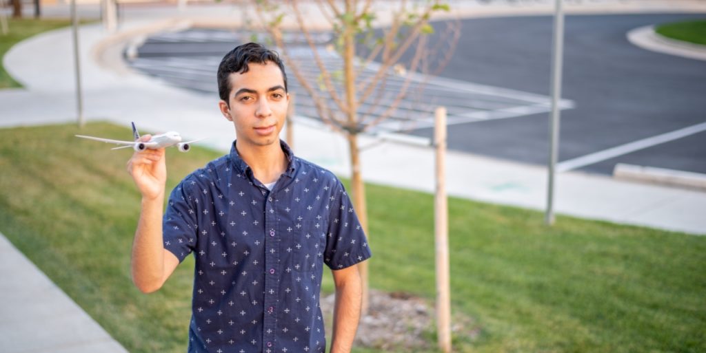 Ricardo, CEC Aurora Graduate. Standing on the sidewalk holding a model plane.