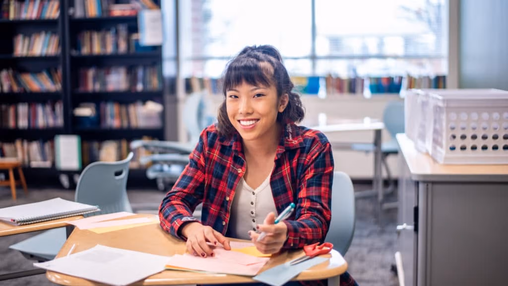 Student sitting in a library at a table studying with books in the background.