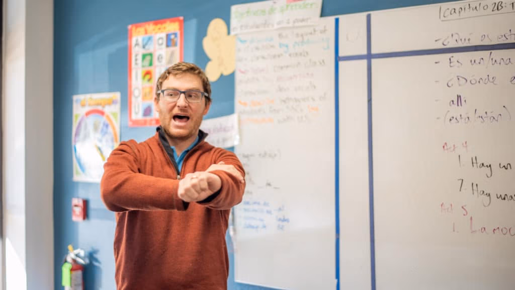 A CEC Teacher rolling up his sleeves in front of a white board in a classroom.