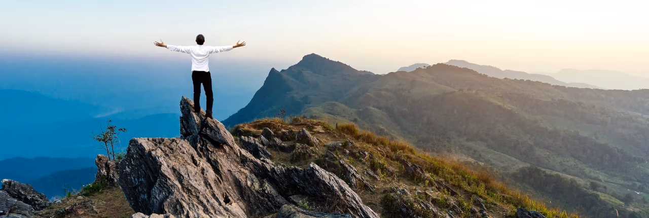 Person standing on the summit of a mountain with their arms outstretched.