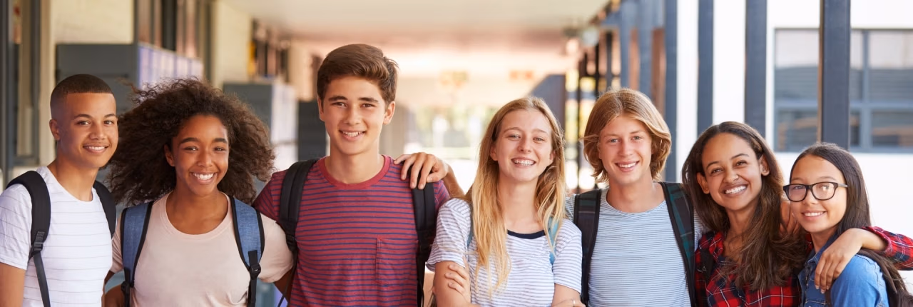 Diverse group of students standing in a line with their arms around each other outside of a school.