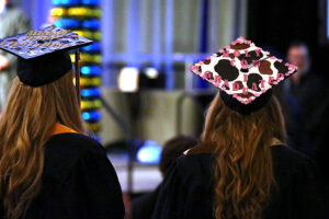 Two graduates from CEC Douglas County North wearing caps and gowns facing away from the camera and looking at the stage.