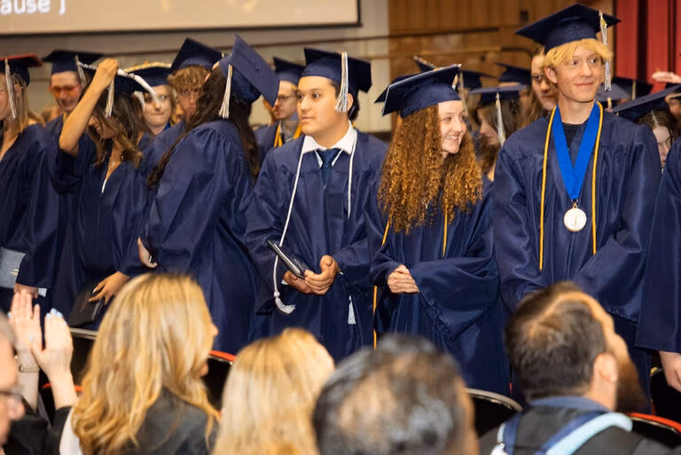 CEC Fort Collins High School graduates in dark blue caps and gowns standing in the Aims Welcome Center.