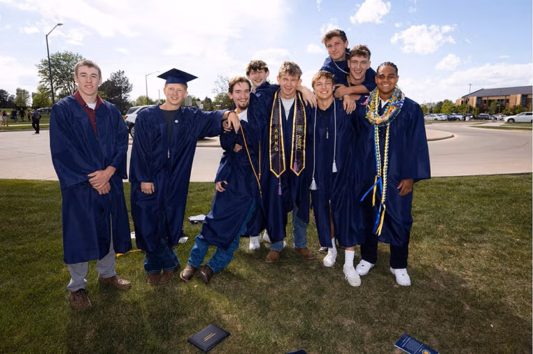 CEC Fort Collins High School graduates in dark blue caps and gowns standing outside after they graduated.