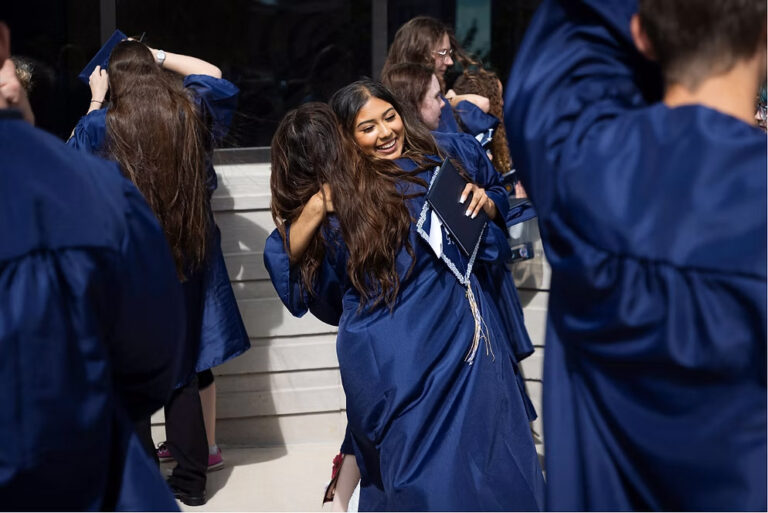 CEC Fort Collins High School graduates in dark blue caps and gowns embrace outside after they graduated.