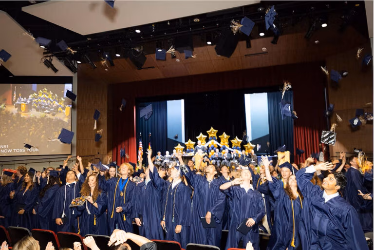 CEC Fort Collins High School graduates standing in a group after they graduated in dark blue gowns throwing their caps in the air.