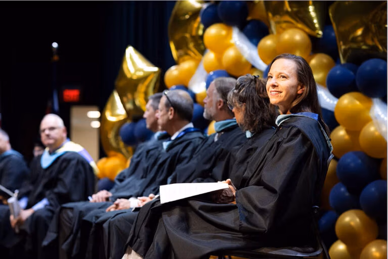 Joliann Beck, Director of Academic & Career Advising looks off into the distance with other faculty in the background at the 2025 CECFC graduation.