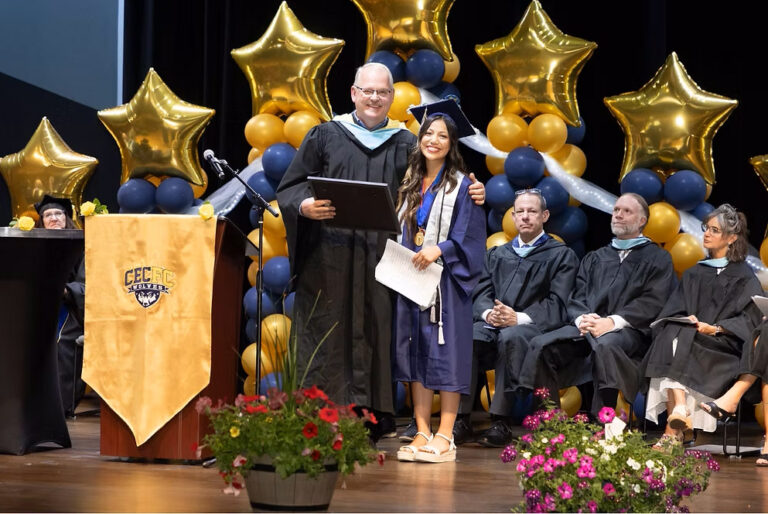 CEC Fort Collins graduate Mera Sanchez receives and award during graduation. There are flowers in the foreground and faculty and balloon in the background.