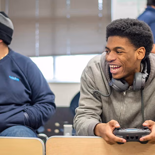 Student laughing with headphones around his neck and a controller in his hands.