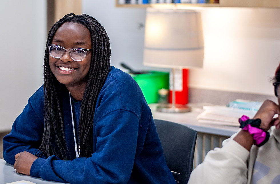 Colorado Early Colleges Aurora student sitting at a classroom desk looking at the camera and smiling.