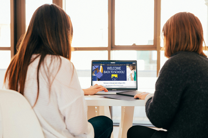 CECA teacher advising a students parent about college options after high school. Both adults are sitting at a table facing a computer.