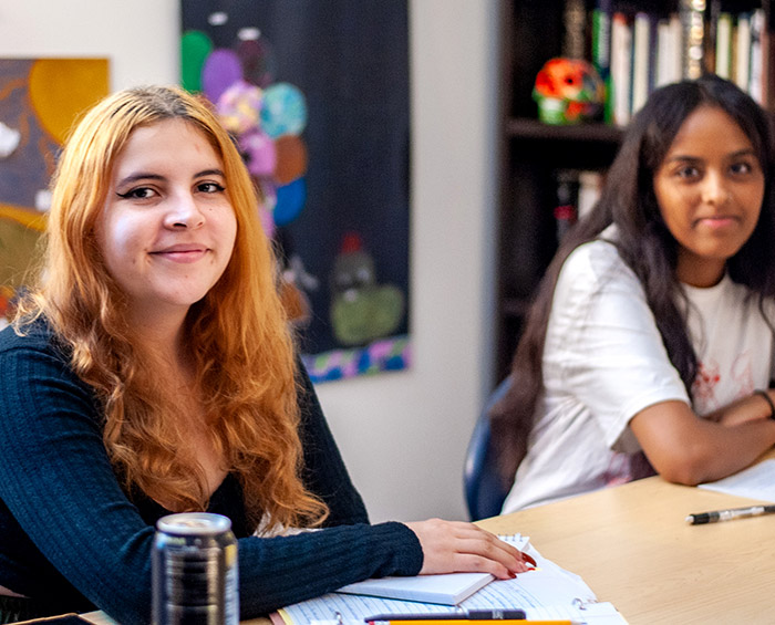 Two students sitting at a desk in a classroom looking at the camera and smiling.
