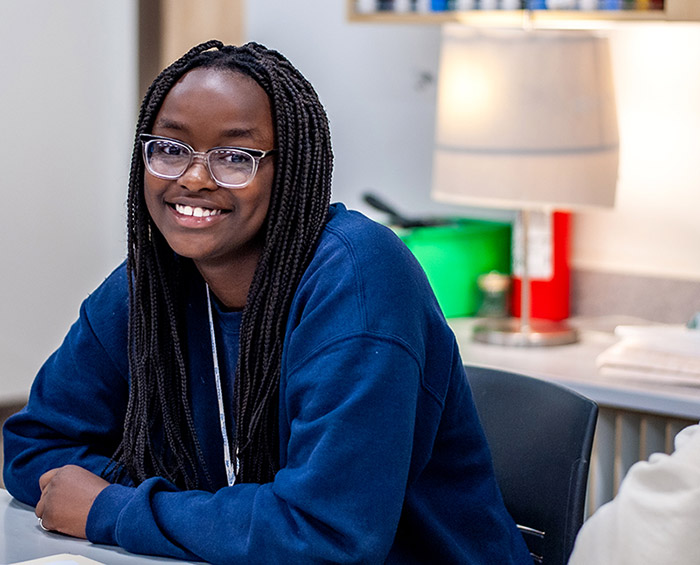 Colorado Early Colleges Aurora student sitting at a classroom desk looking at the camera and smiling.
