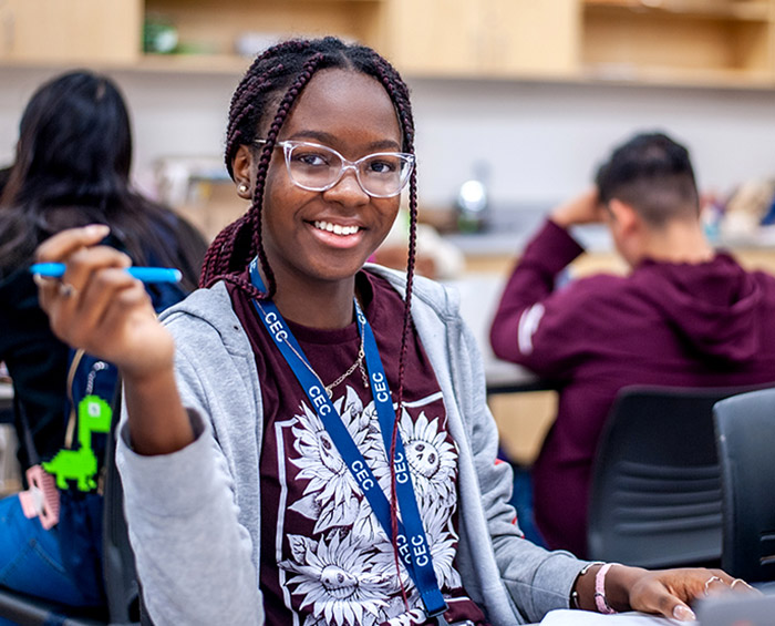 CECA student sitting at a desk, holding a pencil, looking at the camera and smiling.