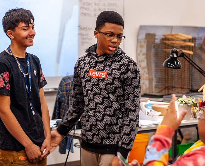 Two students talk with another CECA student after they finish a presentation at the front of the class.