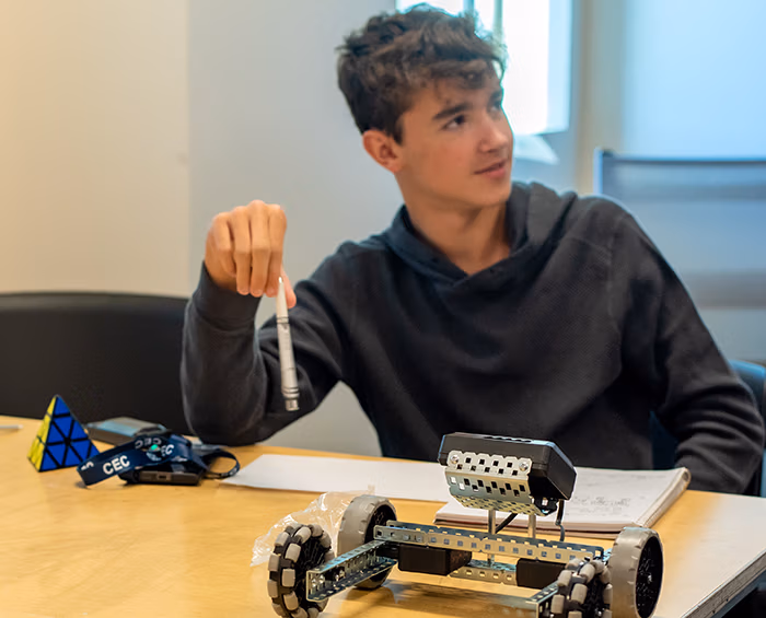 CECCR student sitting at a desk working on a robotics project. There is a robot in the foreground.