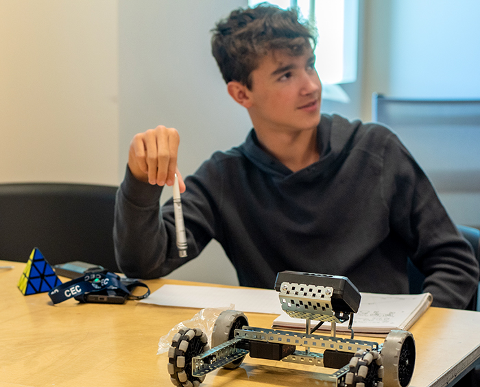 CECCR student sitting at a desk working on a robotics project. There is a robot in the foreground.