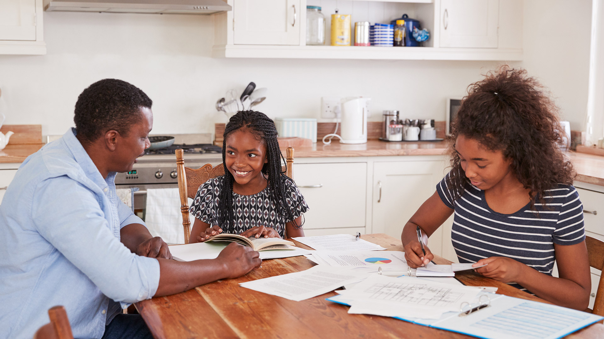 Father helping his two daughters with homework at the kitchen table.