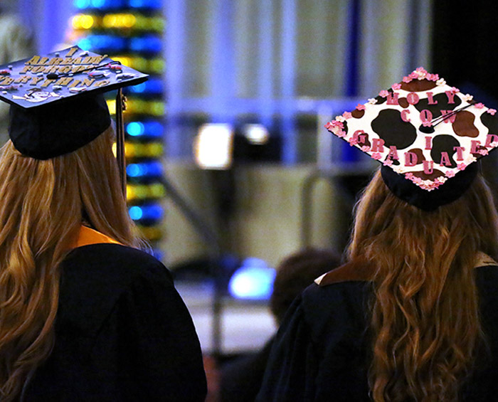 Two CEC DC North students face the stage during graduation. Their caps are decorated in celebration of graduation.