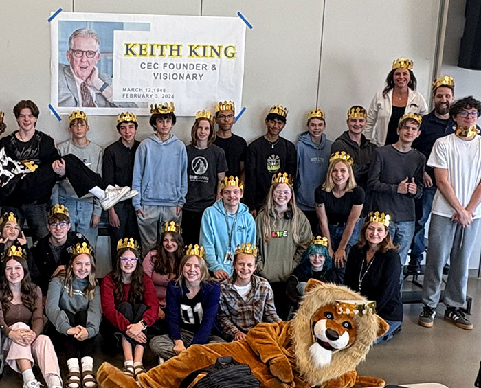 The students at CEC Castle Rock gather for a photo to celebrate Keith King Day. All the students are wearing crowns and a lion mascot is laying in the front.