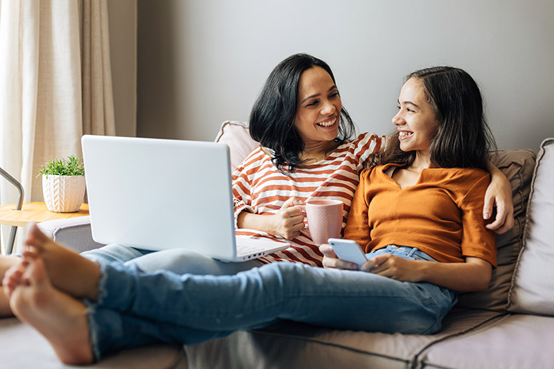 Online-Registration-Event Mother and daughter sitting on a couch with a laptop registering online for Colorado Early Colleges school.