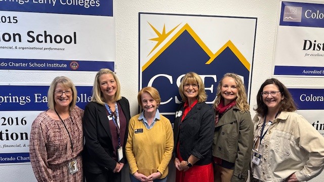 Representative Amy Paschal visits Colorado Early Colleges Colorado Springs. Image of Amy and faculty standing in front of a large CEC logo.