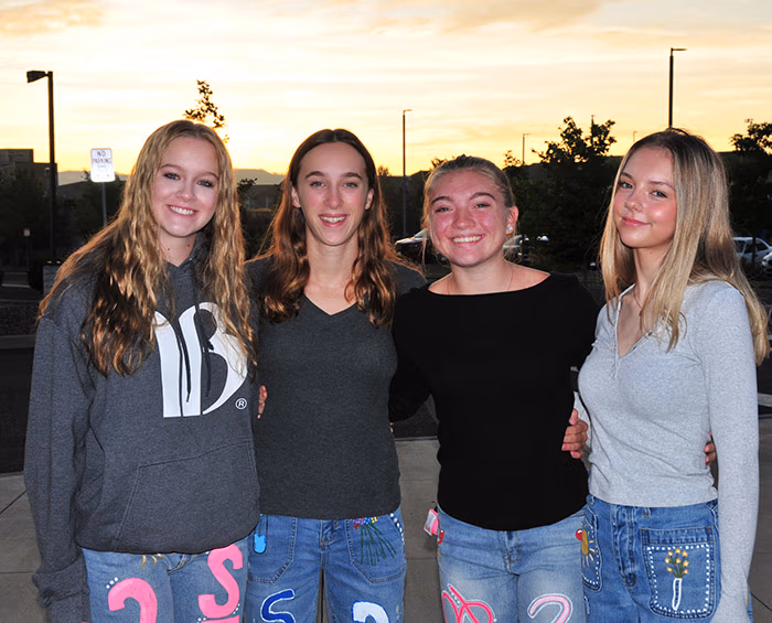 Four CEC Castle Rock seniors at a senior sunrise event, standing in a line looking at the camera with the sun rising in the background.