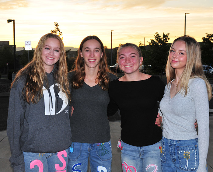 Four CEC Castle Rock seniors at a senior sunrise event, standing in a line looking at the camera with the sun rising in the background.