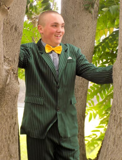 Evan Wilson wearing a green suit and a yellow bow tie, standing between two trees.