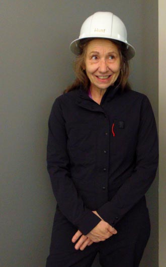 Teacher Ms. Hunt poses for a picture wearing a white hardhat and navy coveralls.