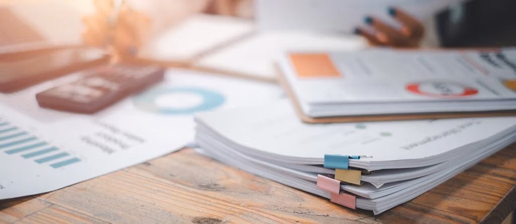 Stacks of papers and a calculator on a desk.