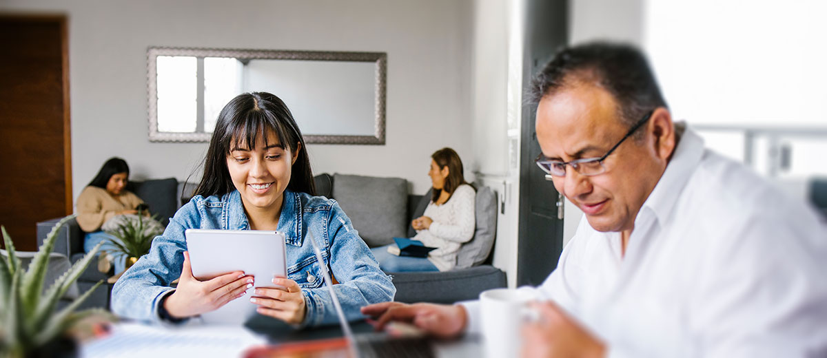 Family working at a table with other family members on the couch in the background.
