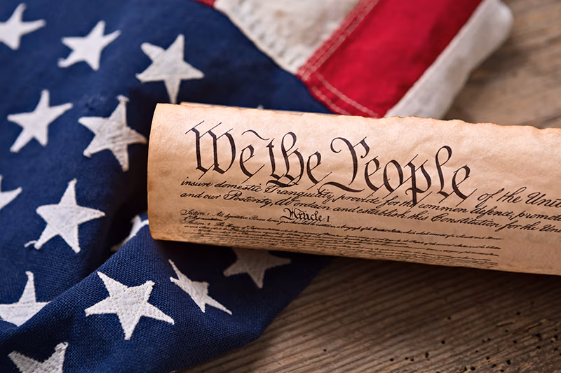United States Constitution, rolled in a scroll on a vintage American flag and rustic wooden board.
